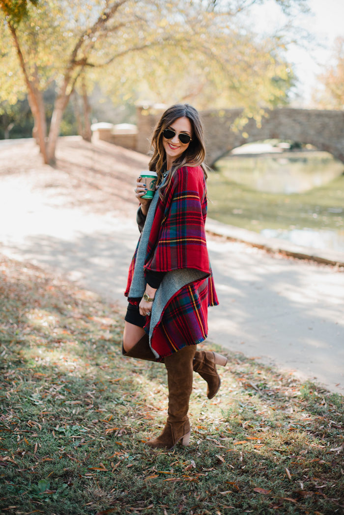 Blogger Mallory Fitzsimmons of Style Your Senses wears a black body con dress as a base layer and a gorgeous reversible poncho over it, finished with chestnut over the knee boots