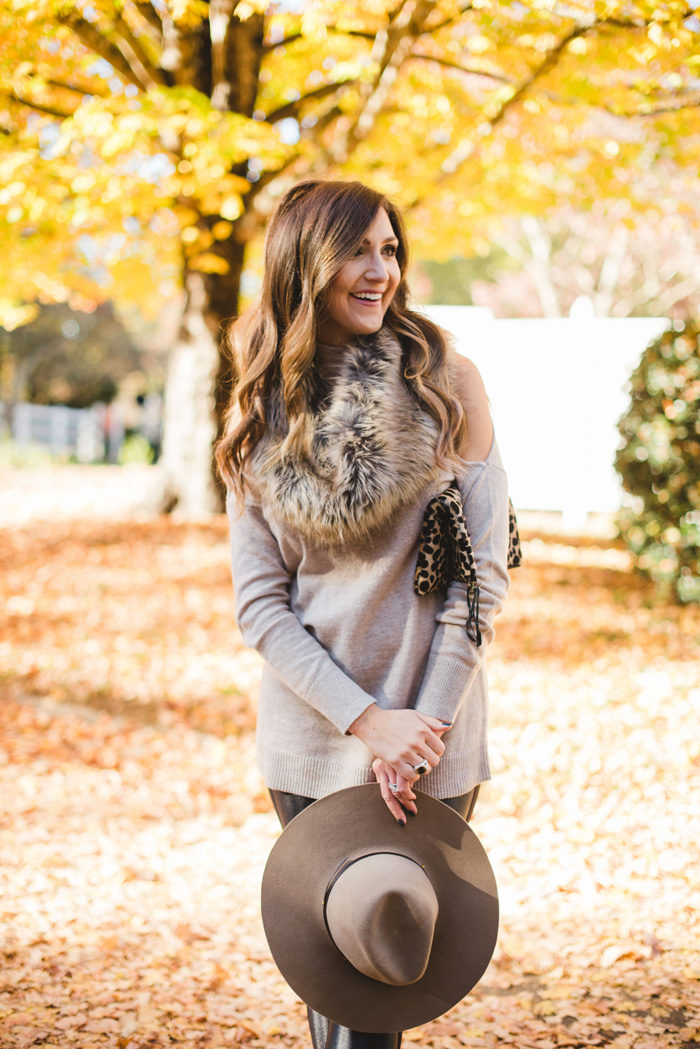 Blogger Mallory Fitzsimmons of Style Your Senses wears a cold shoulder tunic sweater with faux leather leggings, a faux fur infinity scarf and felt hat for a festive Fall and Winter look.