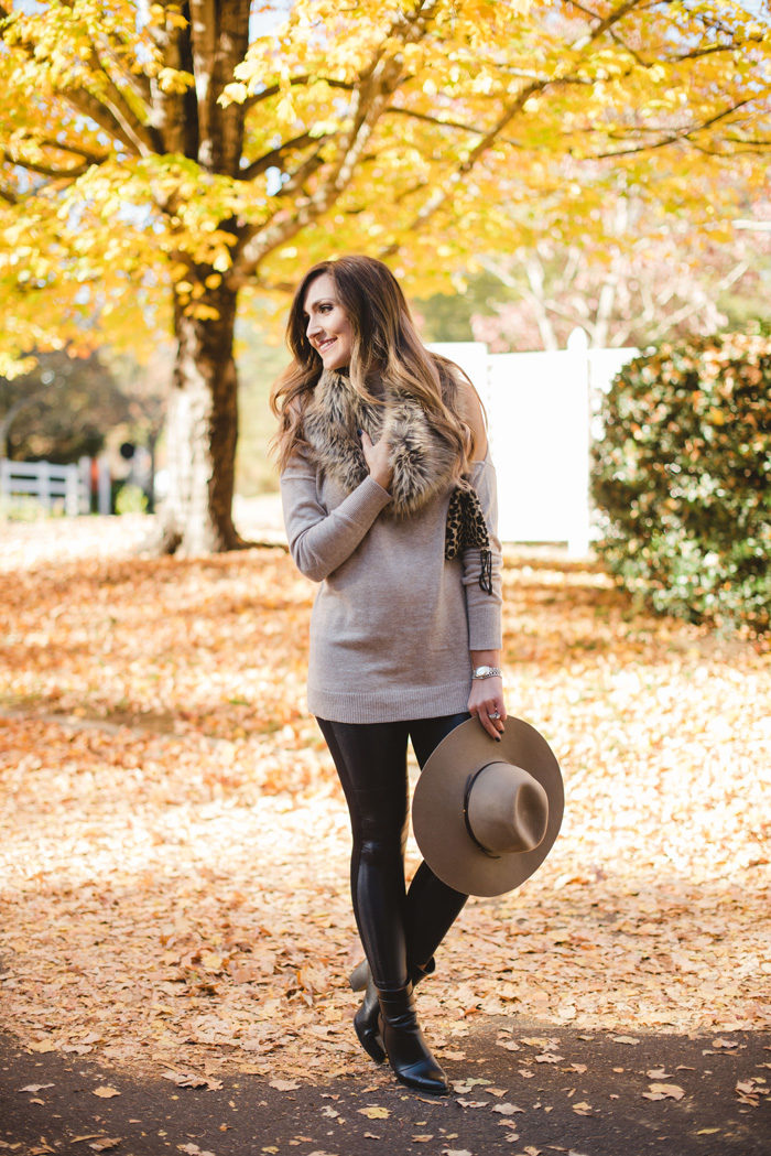 Blogger Mallory Fitzsimmons of Style Your Senses wears a cold shoulder tunic sweater with faux leather leggings, a faux fur infinity scarf and felt hat for a festive Fall and Winter look. 